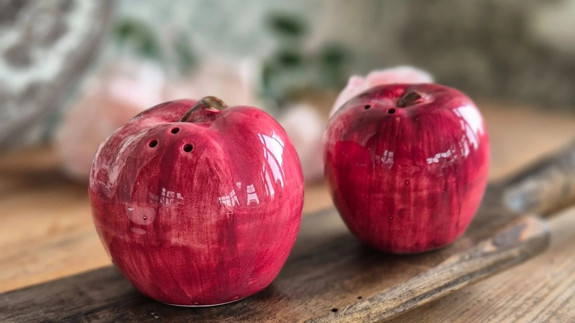 Två dekorativa vintage-äpplen i rött glas på träbord med naturligt ljus i bakgrunden