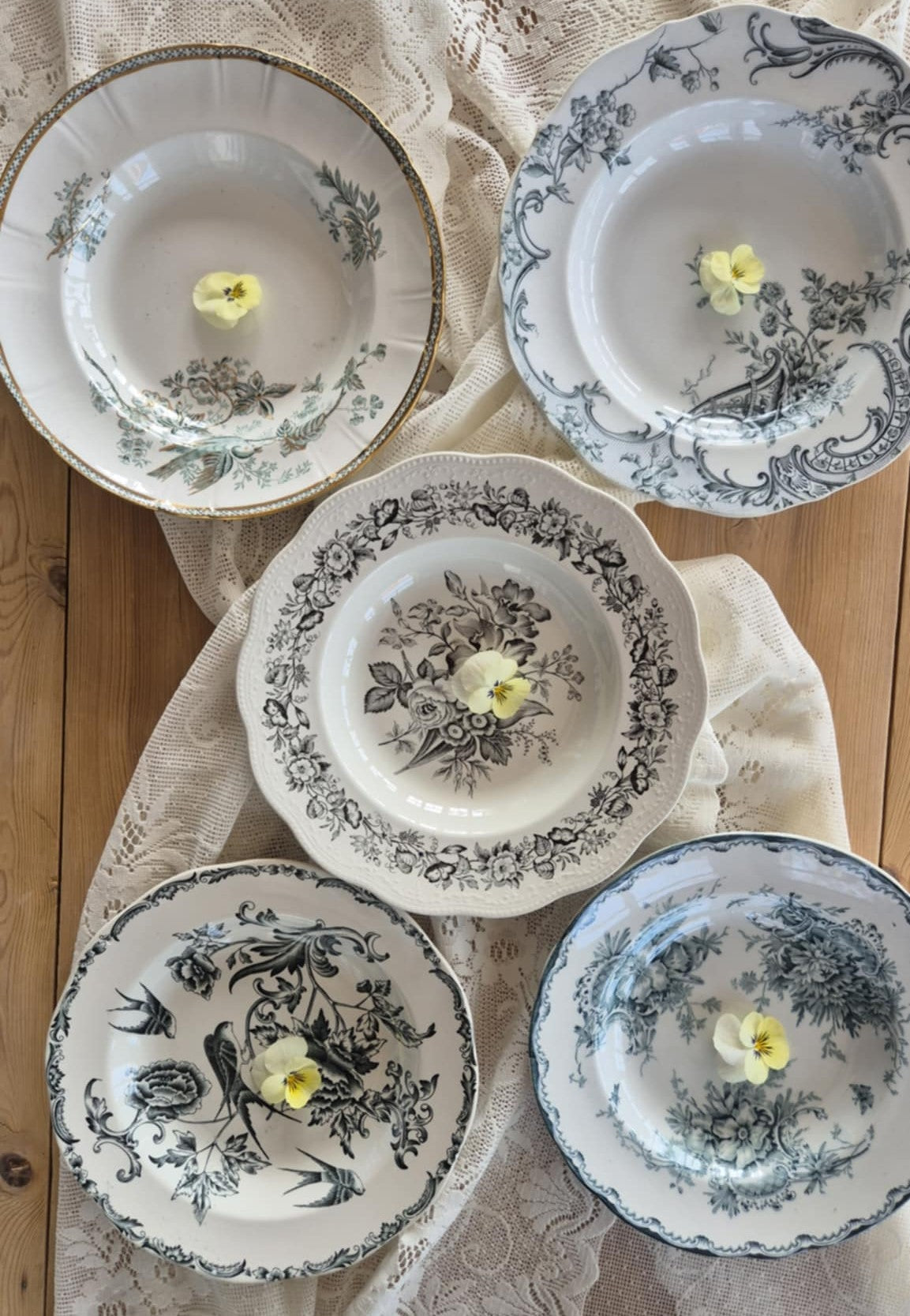 Fem vintage tallrikar med blommönster, fotograferade ovanifrån på ett träbord med gammaldags duk