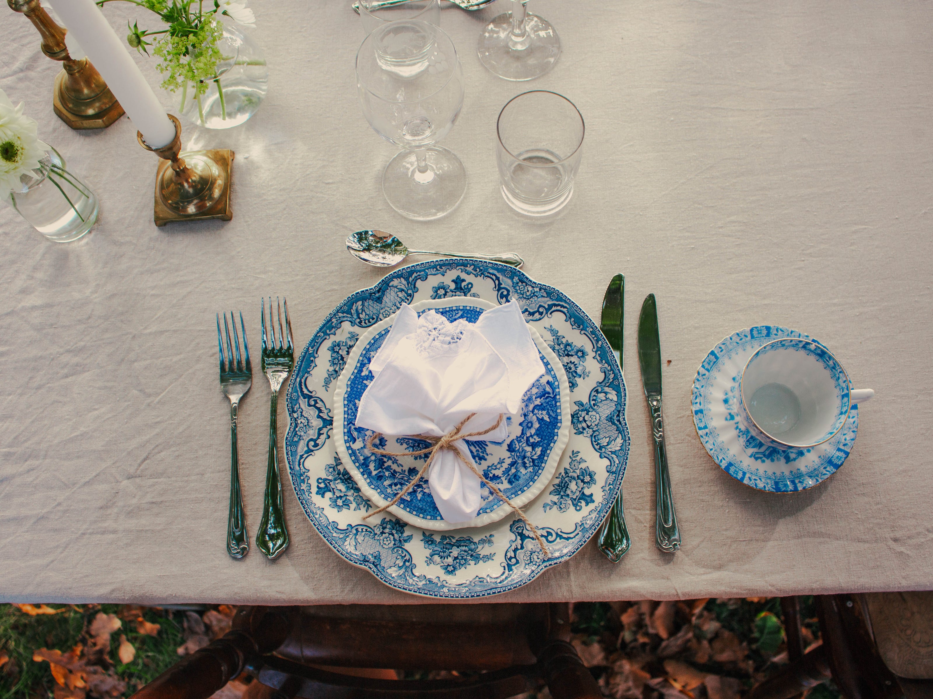Elegant dukning med blåvitt vintageporslin, kristallglas, silverbestick och gröna växter på linneduk.