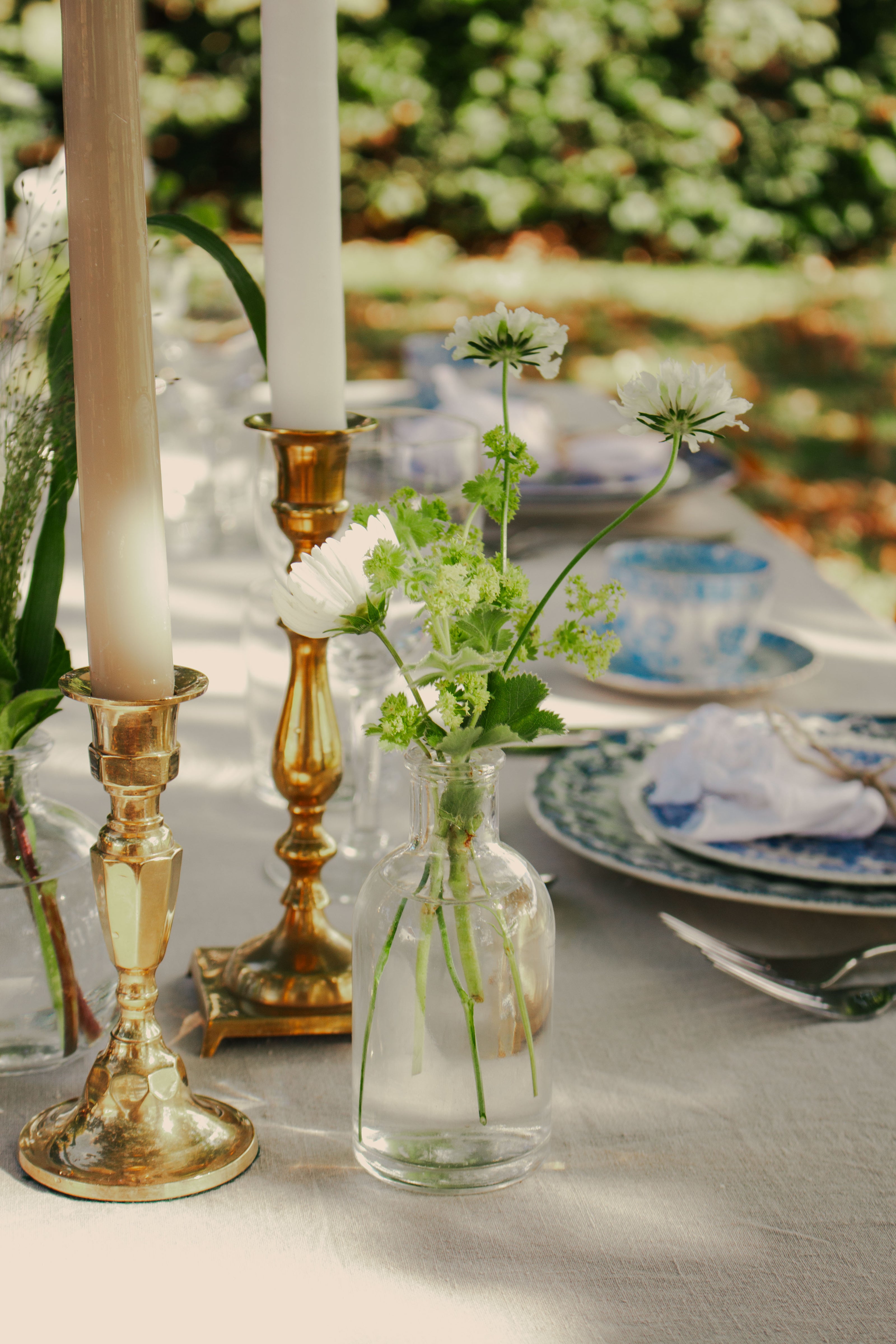 Vintage bordsdukning med gyllene ljusstakar och vita blommor i glasvas, serverad på bordslinneduk med blåvita porslinställ.